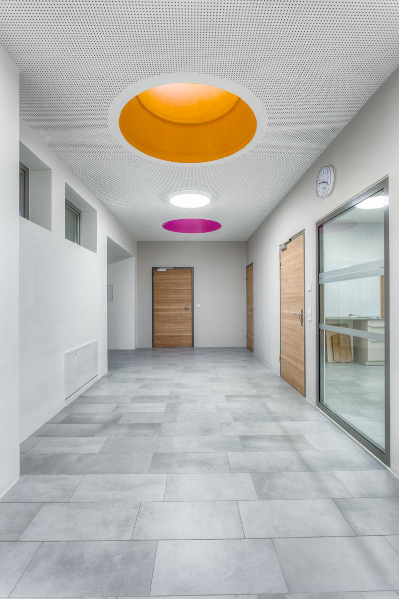 Ein moderner Flur mit grauem Fliesenboden, Holztüren und bunten, runden Oberlichtern in Orange und Rosa, die den Raum erhellen.