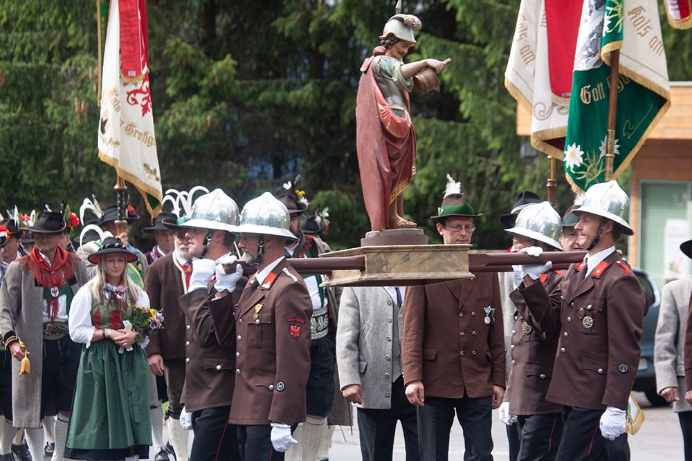 Eine Gruppe von Menschen in traditioneller Kleidung trägt eine Statue während einer feierlichen Prozession.