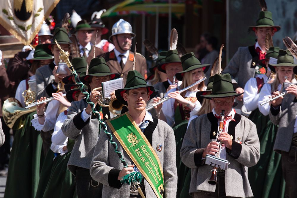 Eine festliche Parade mit Musikern in traditioneller Kleidung, die Blech- und Holzblasinstrumente spielen, umgeben von farbenfrohen Dekorationen.