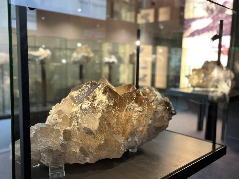 Drei Personen beschäftigen sich in einer Kunstausstellung mit einem farbenfrohen Gemälde einer Berglandschaft und analysieren die Details und die lebendige Szenerie.