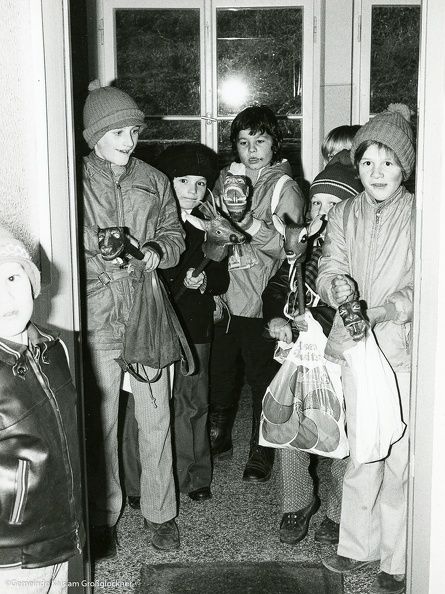 Eine Gruppe warm gekleideter Kinder steht in einer Tür und hält Schnapper und Taschen in der Hand, um einen Moment jugendlicher Begeisterung einzufangen.