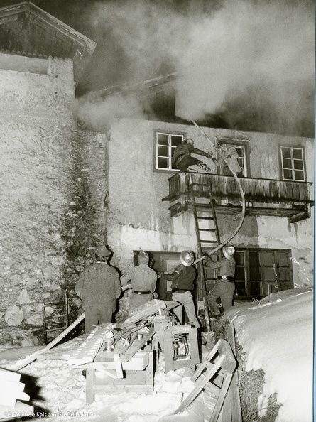Die Feuerwehrleute reagieren auf ein verrauchtes Gebäude und bekämpfen die Flammen in der Nacht mit Schläuchen und Leitern bei Schneefall.