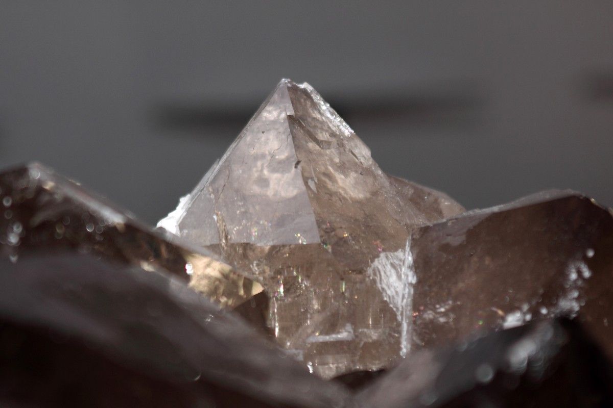 Nahaufnahme eines scharfen, durchscheinenden Quarzkristalls mit einer spitzen Spitze, umgeben von dunklen, strukturierten Steinoberflächen.