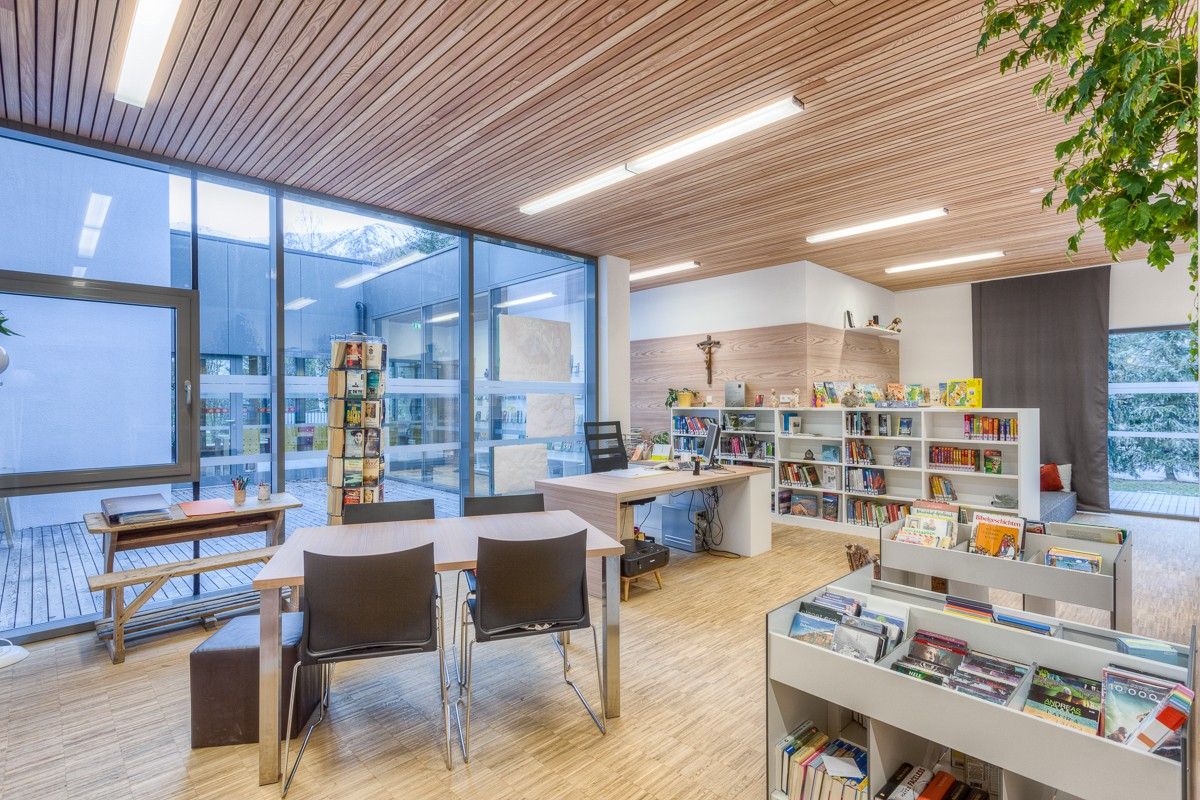 Helle und moderne Bibliothekseinrichtung mit Holzakzenten, Bücherregalen, Schreibtischen und großen Fenstern mit Blick ins Freie.