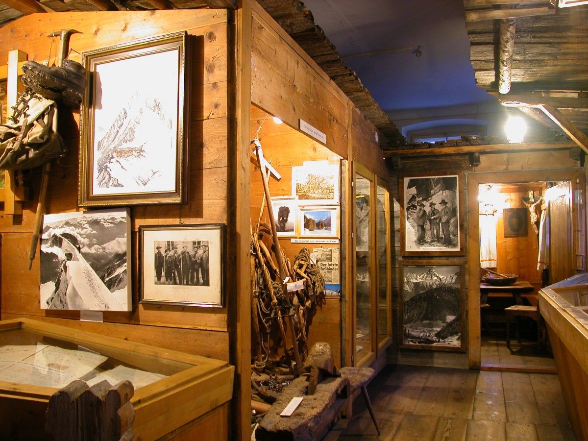 Innenraum eines rustikalen Museums mit Kletterartefakten, historischen Fotografien und Holzexponaten an einer holzgetäfelten Wand.