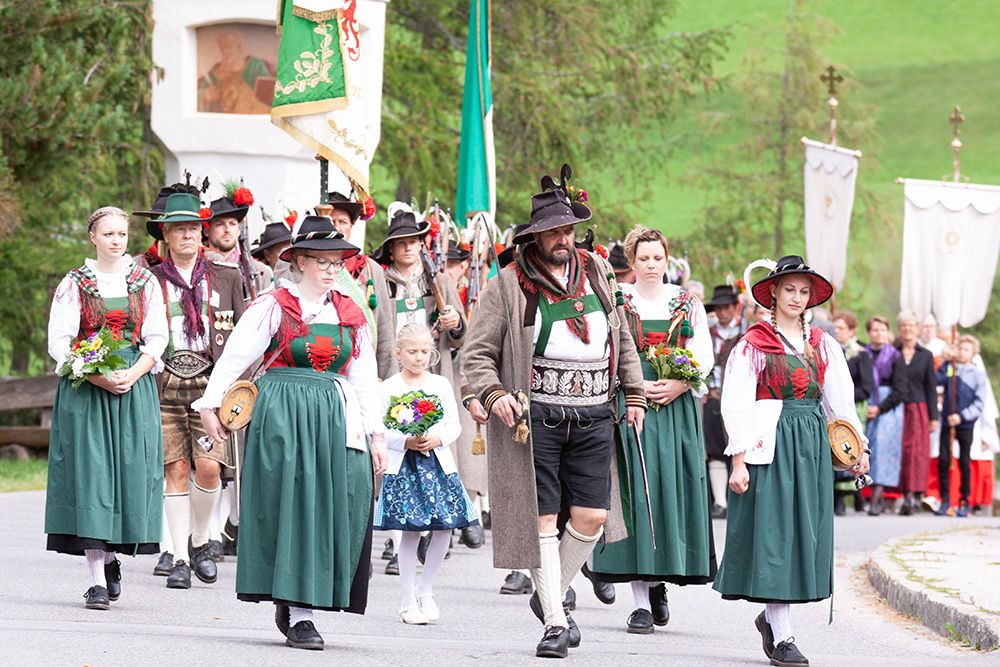 Ein traditioneller Umzug mit Teilnehmern in farbenfrohen regionalen Trachten, die Blumen, Fahnen und verschiedene zeremonielle Gewänder tragen.