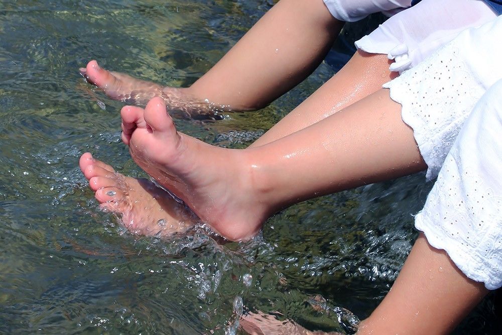 Zwei Paar Füße planschen verspielt im klaren Wasser und fangen einen Moment sommerlicher Freude und unbeschwerten Spaßes ein.