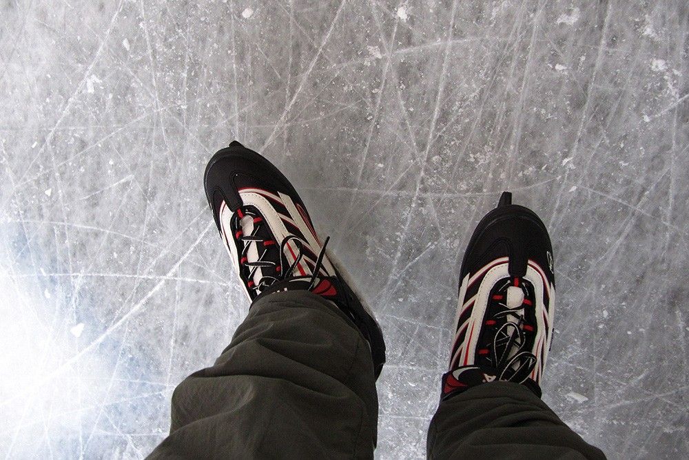 Luftaufnahme von zwei schwarzen und weißen Schlittschuhen auf glattem, strukturiertem Eis mit leichten Kratzern.