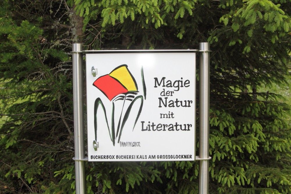 Schild mit der Aufschrift „Magie der Natur mit Literatur“ in der Nähe eines Waldgebiets, das für Natur und Literatur wirbt.
