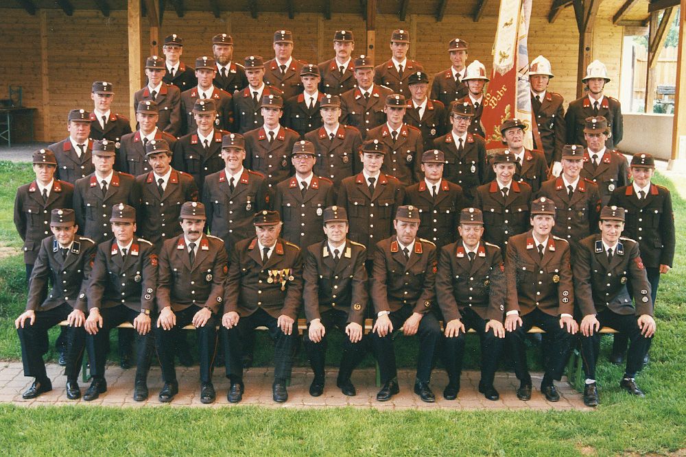 Ein Gruppenfoto von uniformierten Personen, die alle braune Uniformen mit verschiedenen Abzeichen tragen und in geordneten Reihen im Freien stehen und sitzen.