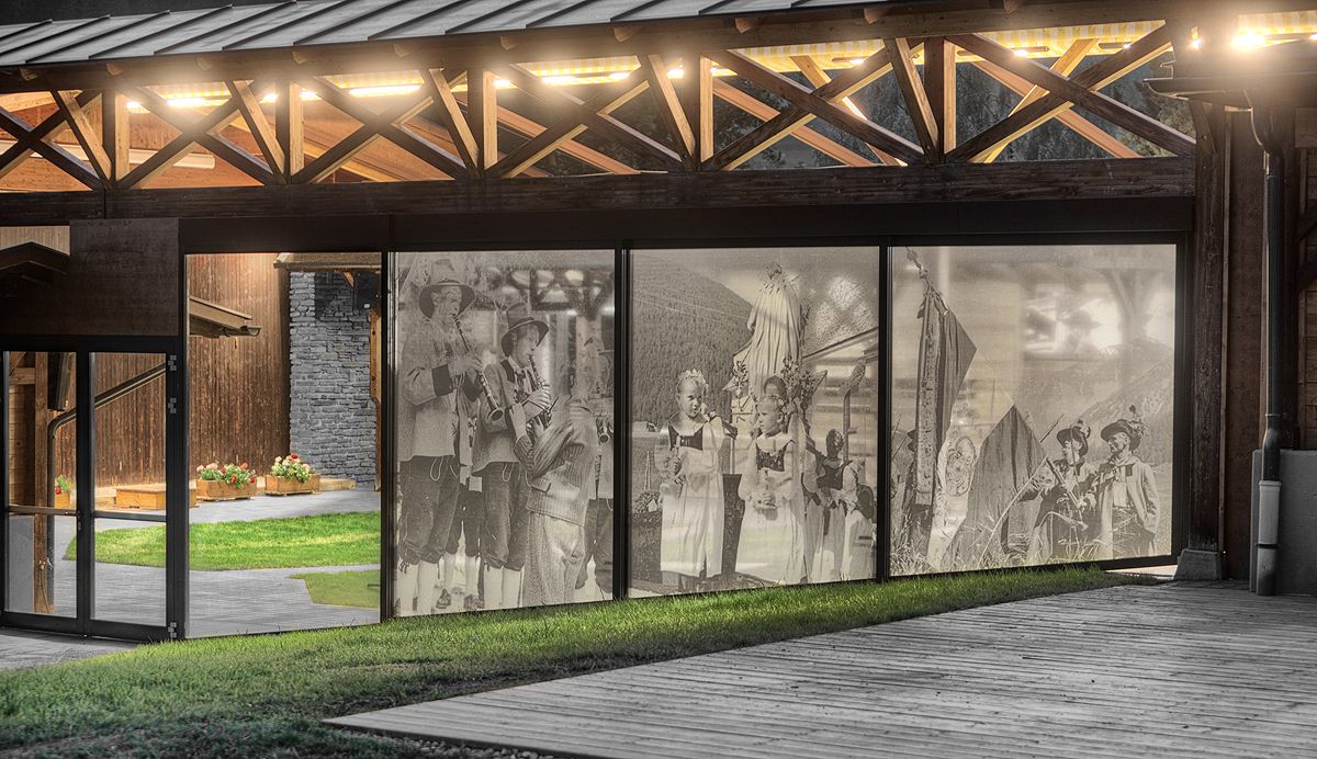 Eine moderne Holzkonstruktion mit großen Glasscheiben, auf denen verblasste historische Bilder von traditionellen Festen und Musikern zu sehen sind.