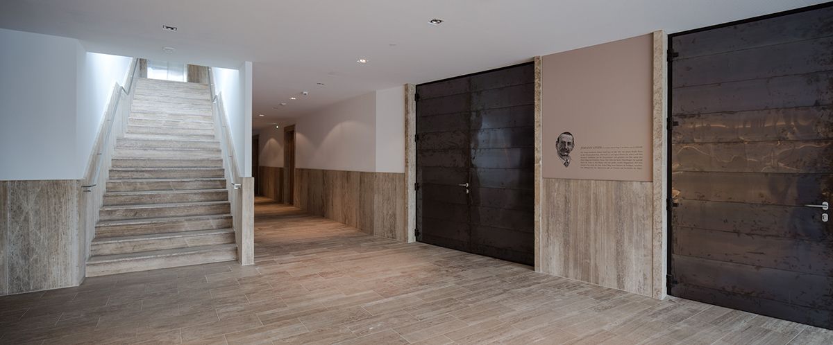 Ein moderner, geräumiger Flur mit einer Treppe, die nach oben führt, Wänden mit Holz- und Metallakzenten und einer neutralen Farbpalette.