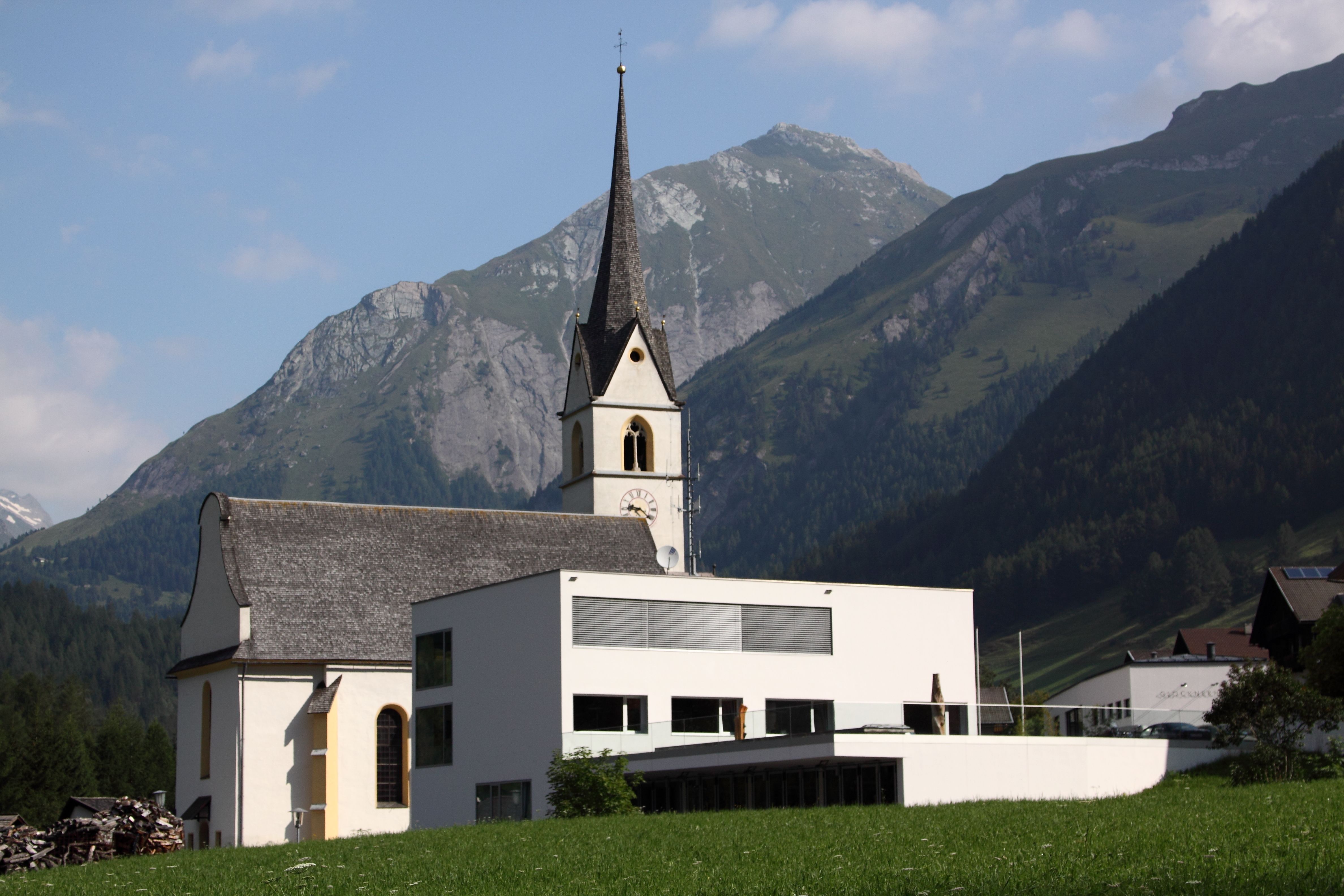 Gemeindeamt im Hintergrund die Kirche und Berge mit blauen Himmel