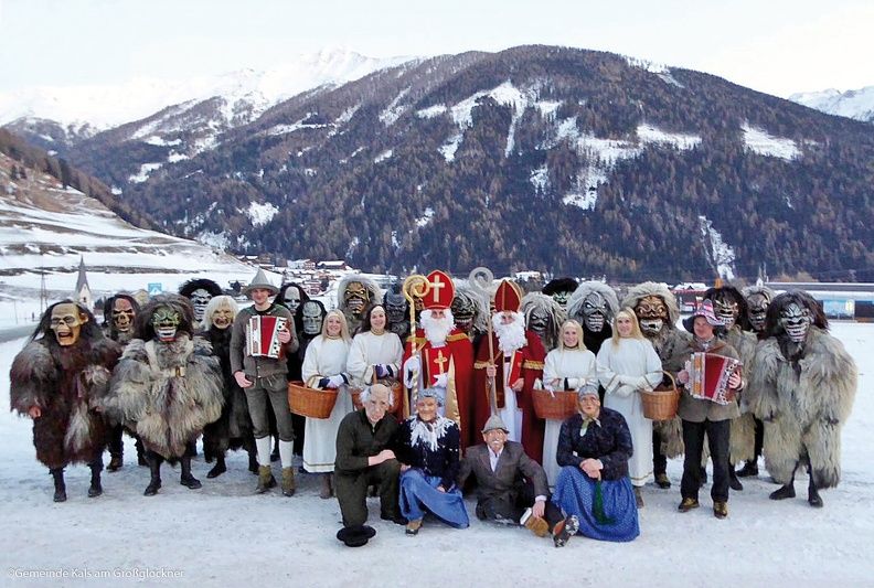 Eine festlich gekleidete Gruppe mit traditionellen Kostümen und Musikinstrumenten posiert vor schneebedeckten Bergen.